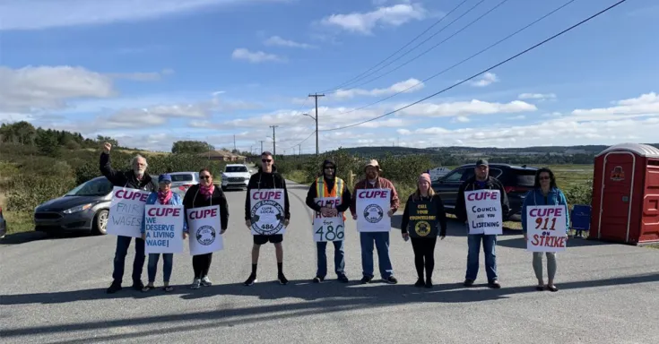 Group of people standing across a road holding picket signs