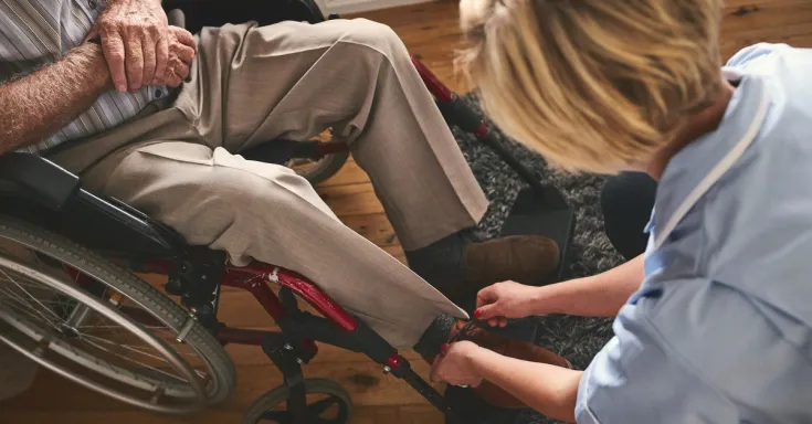 Home care worker tying shoe of man in wheelchair