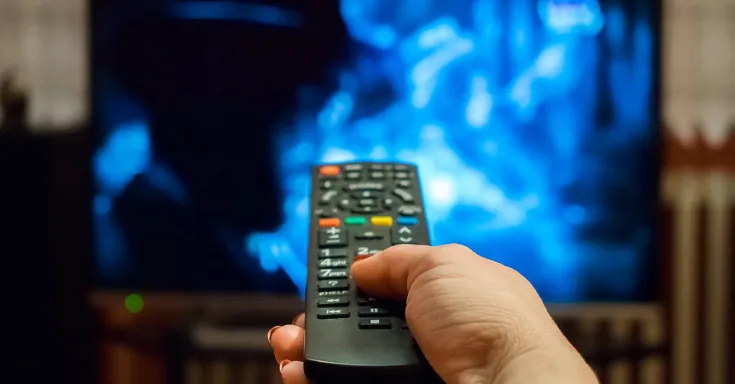 Une main, tenant une télécommande, pointée vers un téléviseur