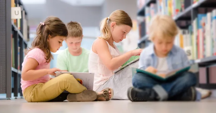 Group of four children sitting on a library floor and reading books