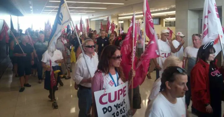 A crowd of mena and women with placards and flags march into a public building