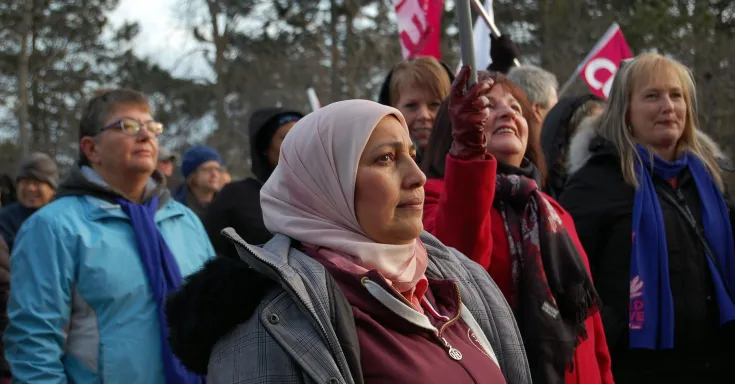 Woman in a light coloured head scarf and winter coat in a crowd of people