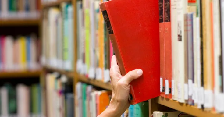 Hand taking a book from a library shelf