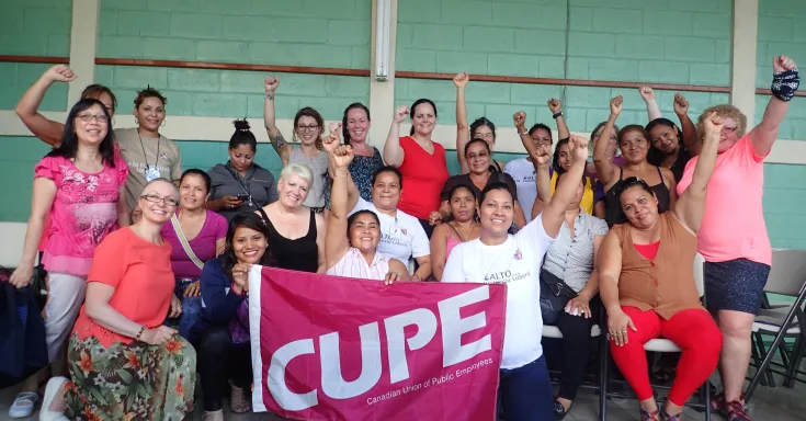 Group of women with raised fists holding a pink CUPE flag