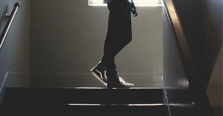 Back lit, person from the waist down standing on the landing of a stair well
